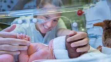 verpleegkundige houdt handje baby in couveuse vast
