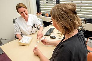 Foto van zorgverlener die patiënt uitleg geeft over gebruik injecties