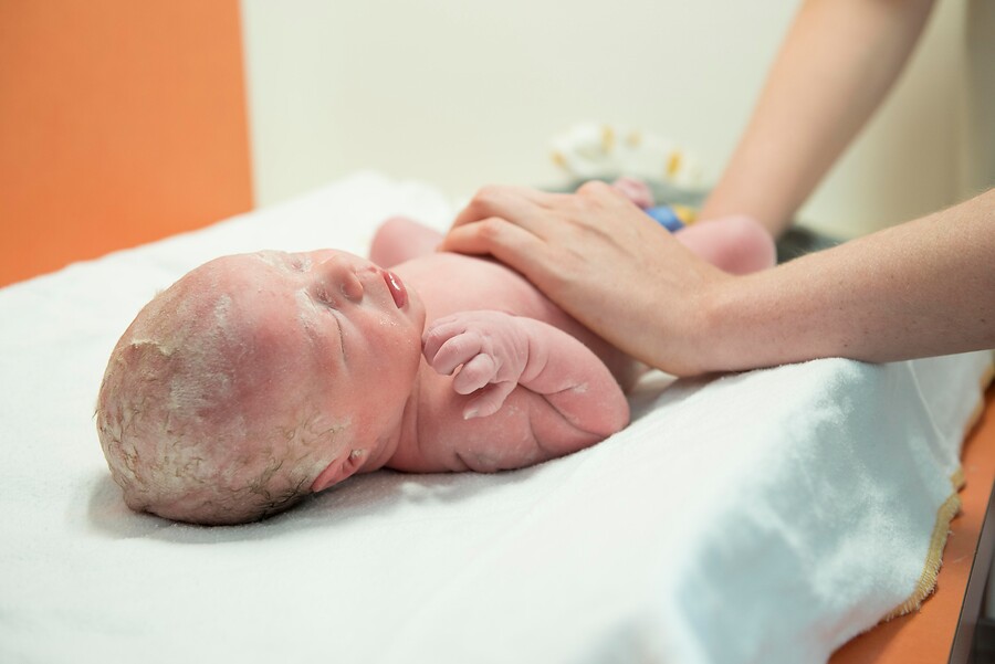 Pas geboren baby op het aankleedkussen die vastgehouden wordt door verpleegkundige