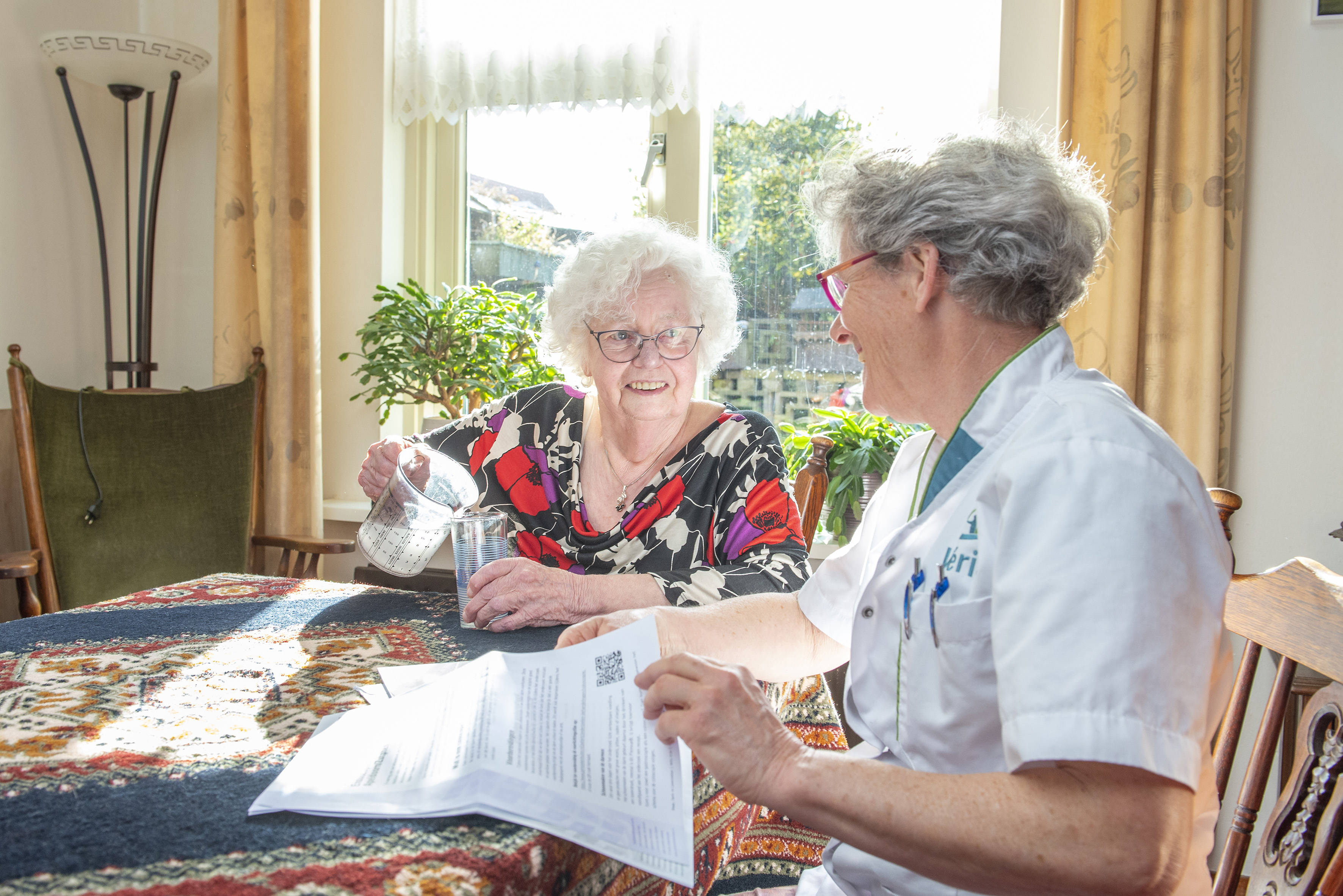 Patient schenkt aan tafel laxeermiddel in, onder toeziend oog van de verpleegkundige van Vérian